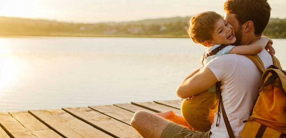 A young boy hugs his dad n on a dock over the water.